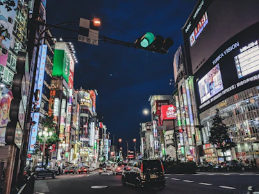 A vibrant city street at night, glowing with neon signs and bustling with life.