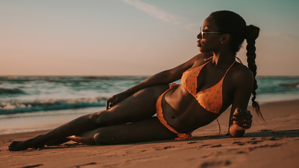 woman wearing bikini while lying on sand by the seashiore