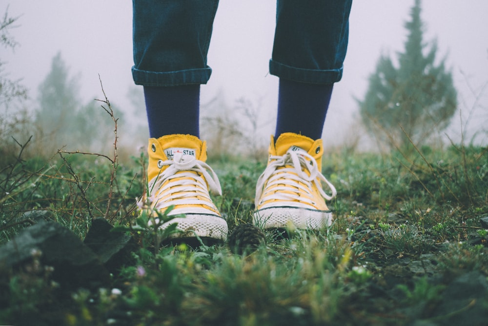 person in black pants and yellow sneakers standing on grass field