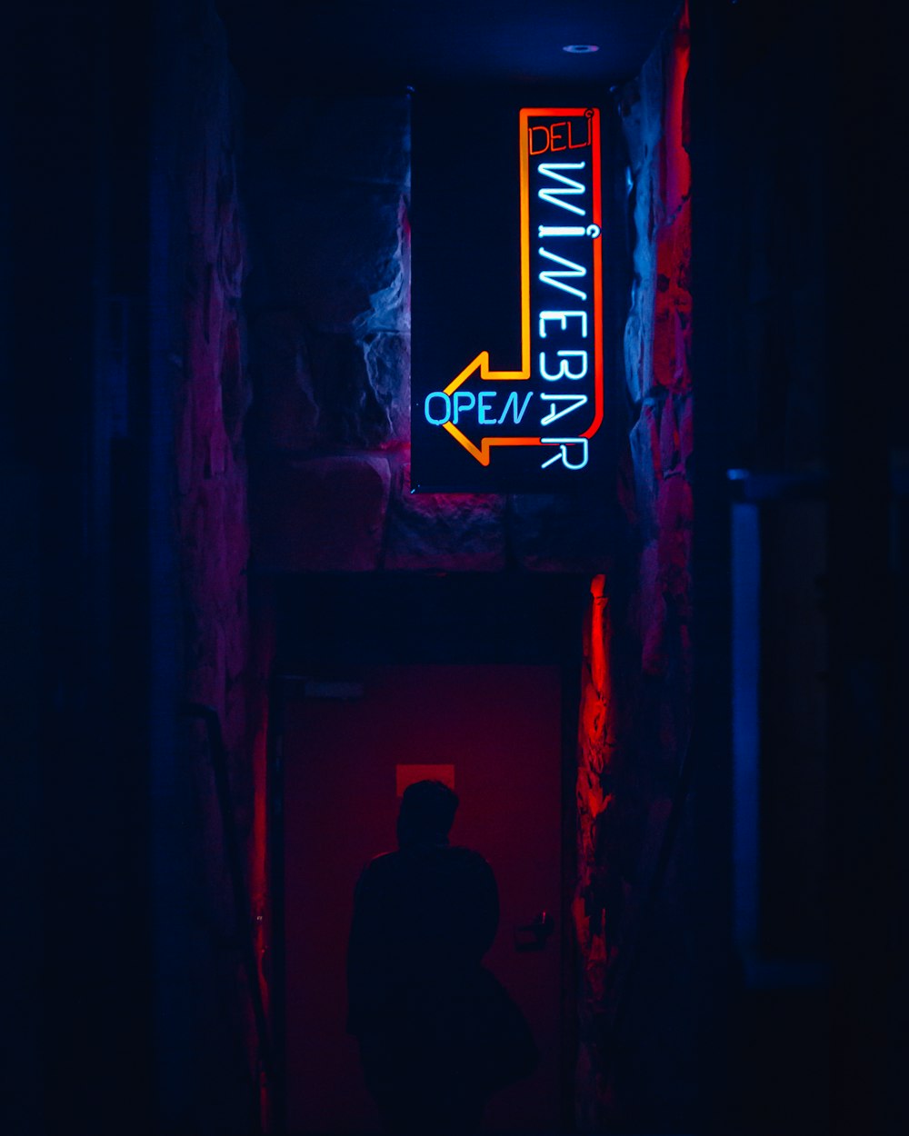 a person standing in a dark hallway with a neon sign