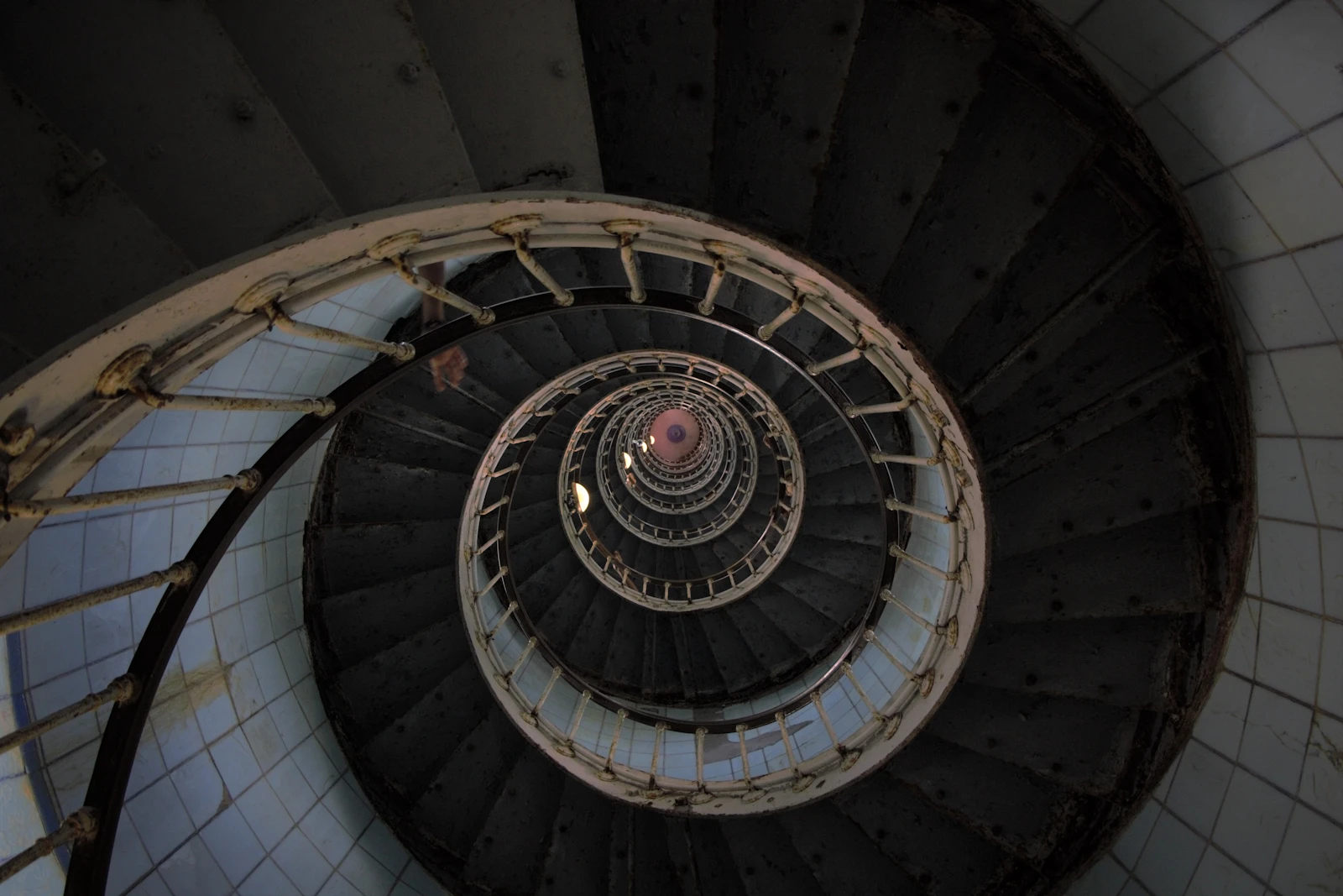 Dark spiral staircase seen from above, its stone steps winding downward in a high-contrast circular pattern of black and grey