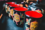 A set of beautifully decorated black ceramic cups with intricate Asian-inspired designs in red and gold. The interiors of the cups are vividly colored in red, creating a striking contrast with the black exteriors. The cups are arranged elegantly, suggesting a traditional tea setting.
