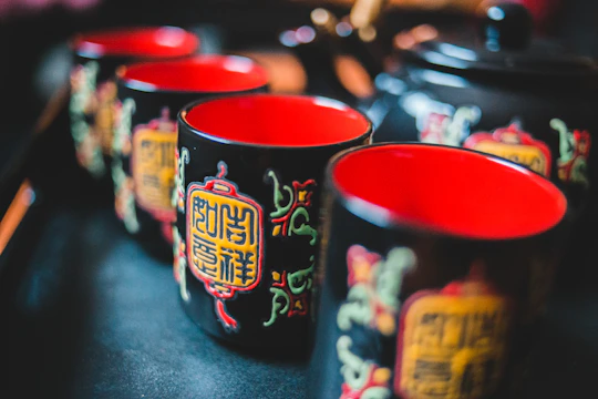 A set of white ceramic mugs featuring sleek red and black Japanese-style artwork on a minimalist background.