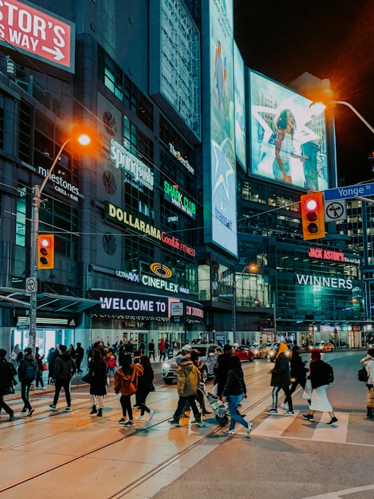 people walking and passing on pedestrian lane near high-rise buildings and different vehicles on road during night time in Yonge St At Dundas St East Canada