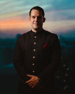 A close-up of a man wearing a sleek black thobe with subtle embroidery, standing confidently against a city backdrop at dusk.