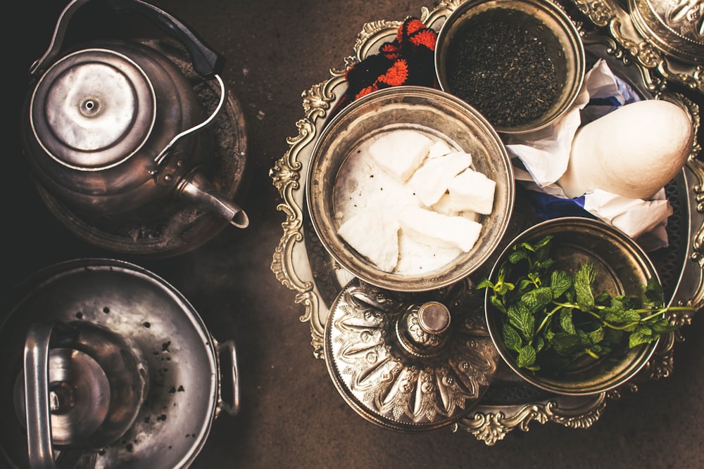 food in bowl near green vegetable in another bowl beside gray stainless steel kettle