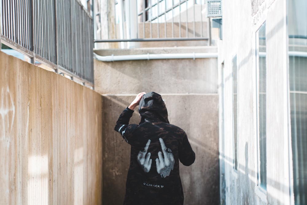 person wearing hoodie standing beside wall