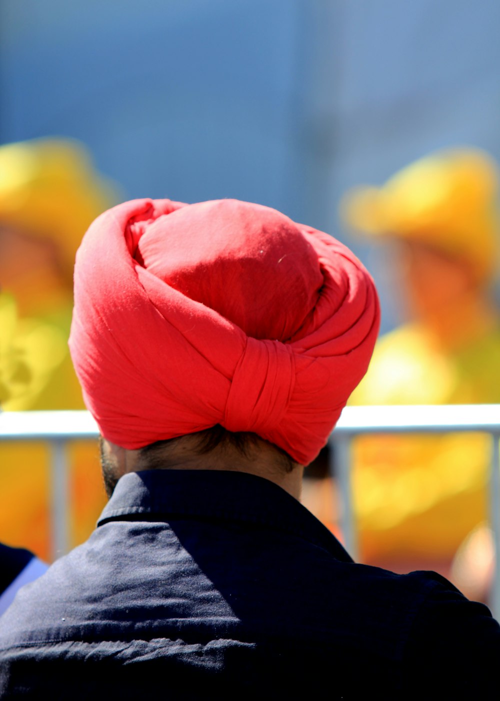 Homem com turbante vermelho virado para trás perto de grades