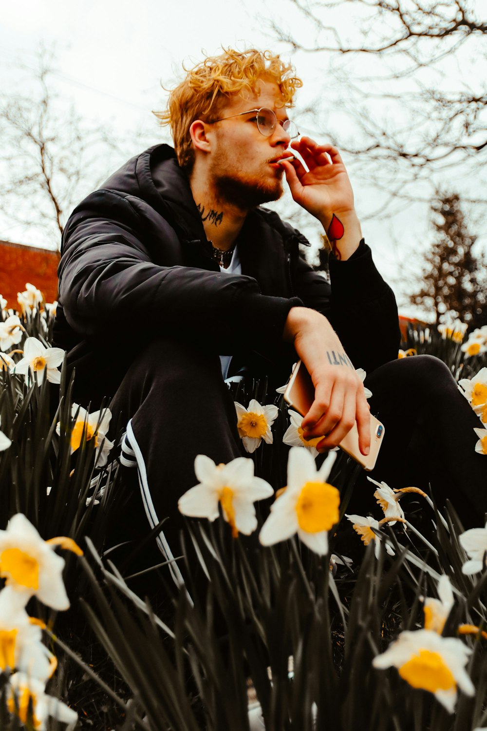 man smoking sitting beside daffodils-flowers during daytime