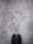 Graffiti art on a concrete surface features a minimalistic line drawing of a face with a bow tie, labeled with the name 'Paul Richard'. The image includes a pair of black shoes at the bottom, indicating a person standing above the artwork.