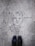 Graffiti art on a concrete surface features a minimalistic line drawing of a face with a bow tie, labeled with the name 'Paul Richard'. The image includes a pair of black shoes at the bottom, indicating a person standing above the artwork.