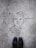 Graffiti art on a concrete surface features a minimalistic line drawing of a face with a bow tie, labeled with the name 'Paul Richard'. The image includes a pair of black shoes at the bottom, indicating a person standing above the artwork.