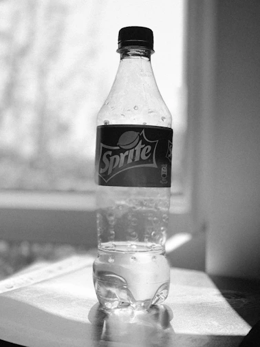 A clear plastic bottle filled with sparkling water, droplets of condensation on the surface.
