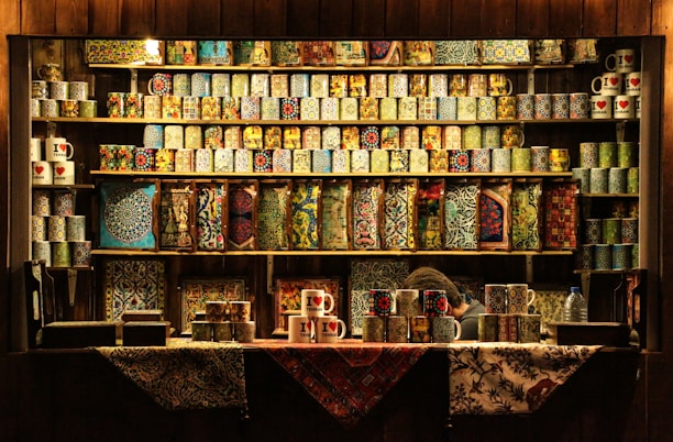 Close-up of colorful custom mugs and azulejos displayed on a wooden shelf.
