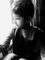 A child in a navy tailored coat standing by a large window with soft natural light.