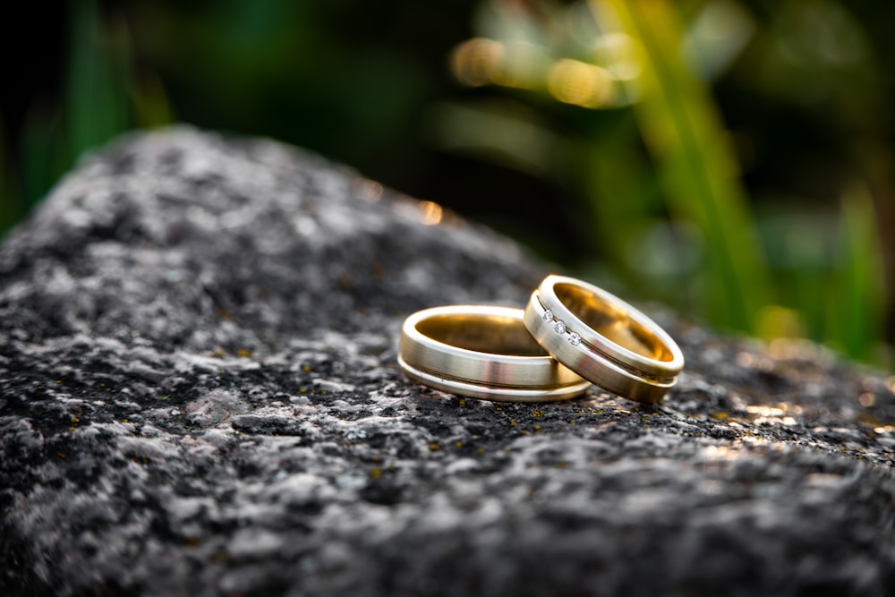 Fotografia de foco seletivo de dois anéis dourados em pedra preta durante o dia