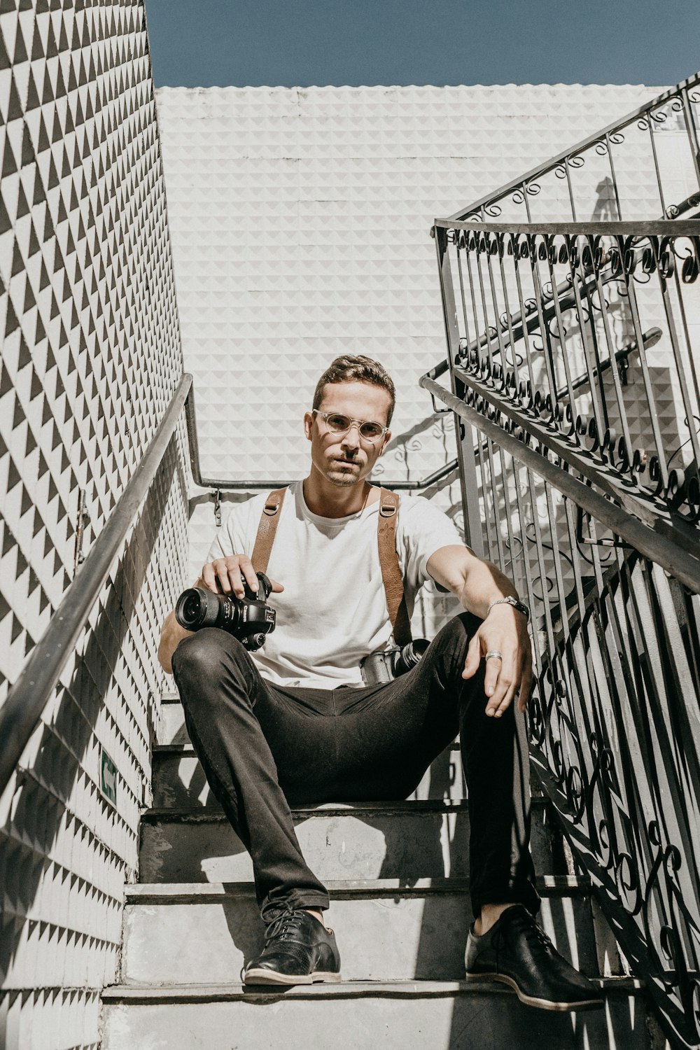 man in white shirt sitting on stairs holding camera