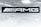 A black sign displays the letters 'AMG' in bold white font. Above it is a metallic, grid-patterned ceiling with modern recessed lighting fixtures. The scene gives an industrial and sleek aesthetic.