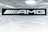 A black sign displays the letters 'AMG' in bold white font. Above it is a metallic, grid-patterned ceiling with modern recessed lighting fixtures. The scene gives an industrial and sleek aesthetic.