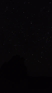 the night sky with stars above a mountain