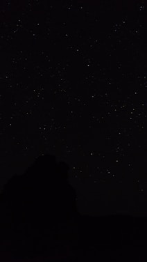 the night sky with stars above a mountain