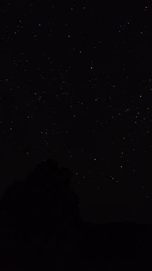 the night sky with stars above a mountain