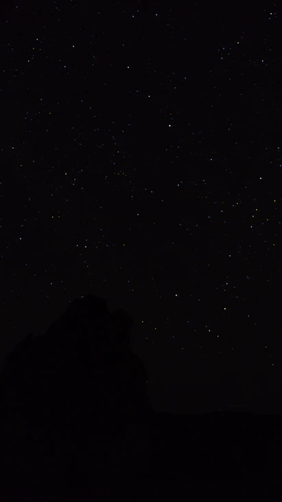 the night sky with stars above a mountain