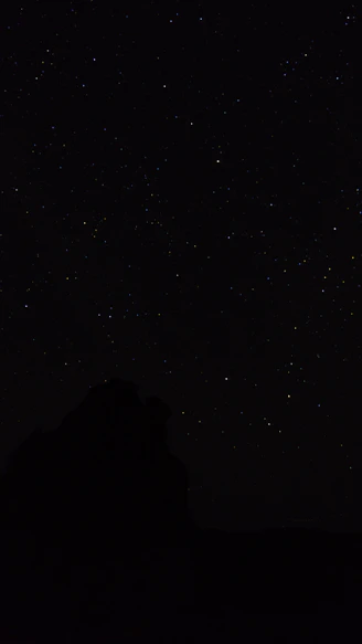 the night sky with stars above a mountain