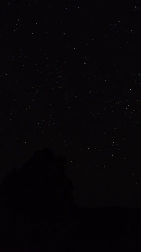 the night sky with stars above a mountain