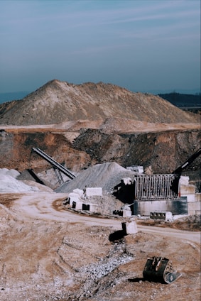 A rugged quarry site with heavy machinery breaking basalt rock under a clear sky.
