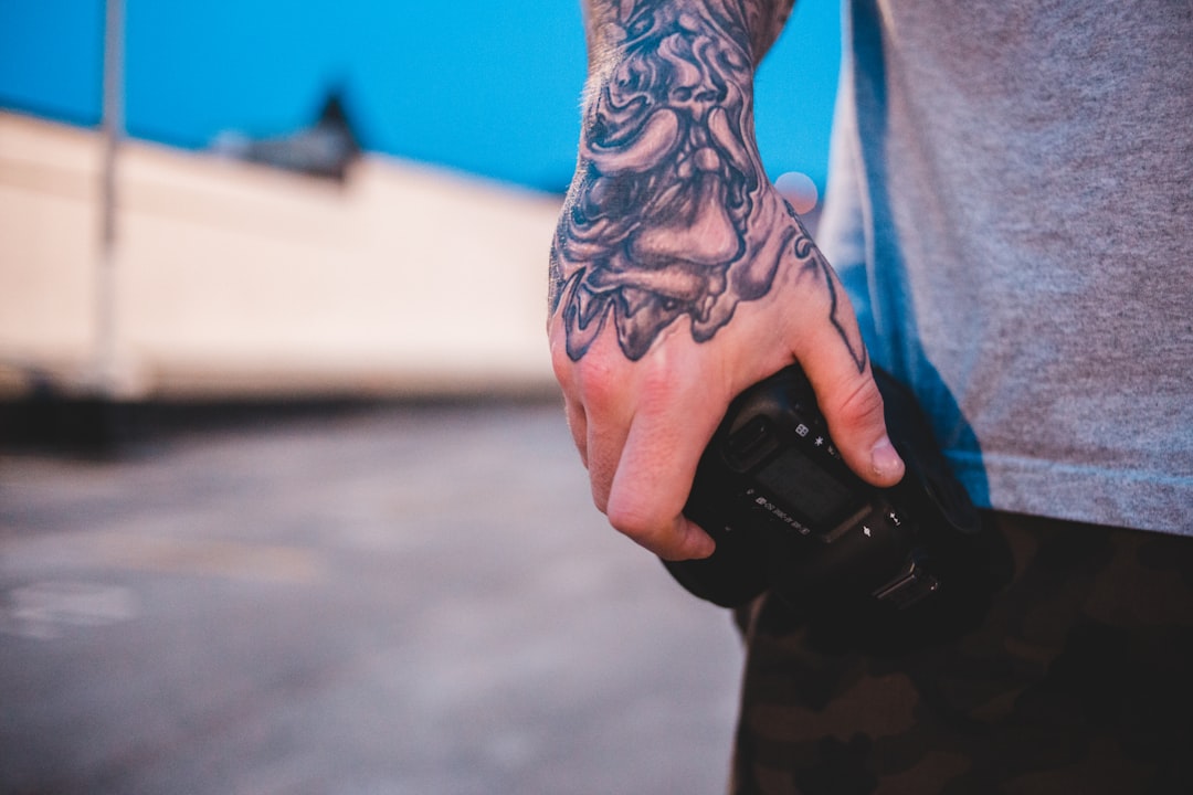 man with tattooed hand holding DSLR camera