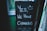 A chalkboard sign with the message 'Yes, we have cannabis' and a smiley face drawn above it. It is propped up outside a building with green walls.