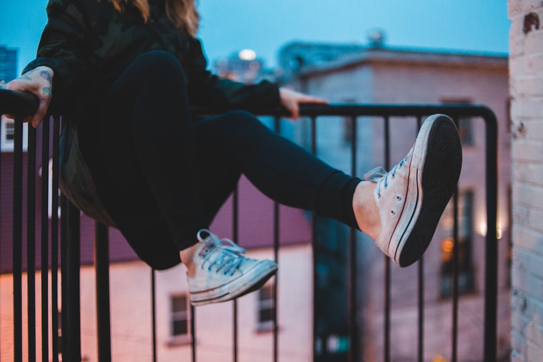 woman wearing white shoes sitting on black railing