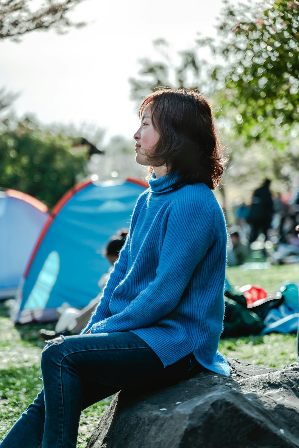 woman in blue sweater sitting on rock