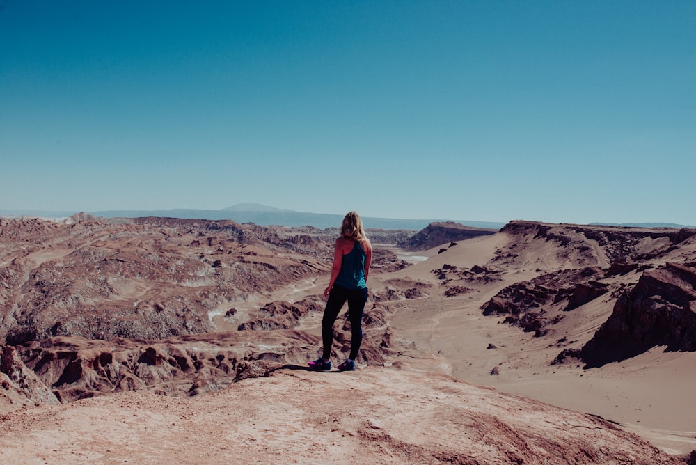Mujer en vestido negro en la cima del cañón mirando el terreno montañoso durante el día