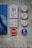 The image depicts several signs mounted on a textured wall. There is a set of signs with the number 31, and graphics representing possibly a hotel or guest service notation. Accompanying them are icons for luggage, utensils, and drinks, suggesting services like accommodation or dining. A red stop sign and a blue parking sign with arrows hint at transportation or traffic indications. The wall is painted with a distressed, artistic finish, and part of a blue poster is visible.