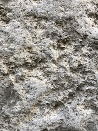 A close-up view of a rough, textured stone surface with uneven, small protrusions and pits giving it a rugged appearance.