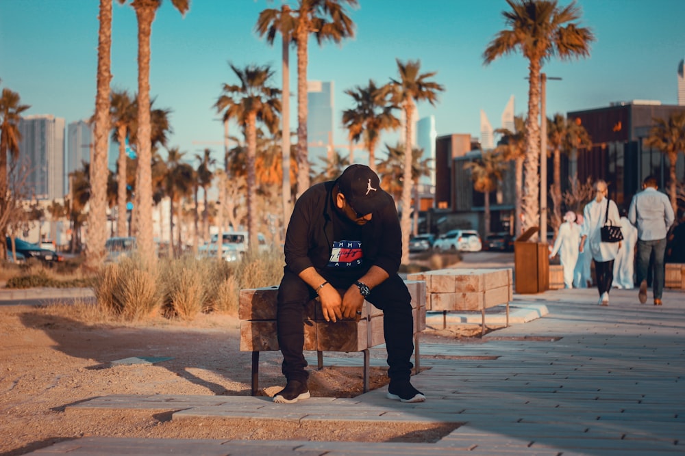 man sitting on bench near palm trees during daytime