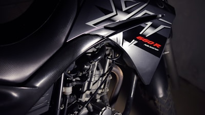 Close-up view of a motorcycle with a focus on its sleek black design featuring bold angular patterns and the label '660R Fuel Injection' highlighted in red. The image emphasizes the mechanical components, showcasing the engine and part of the exhaust.