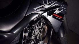Close-up view of a motorcycle with a focus on its sleek black design featuring bold angular patterns and the label '660R Fuel Injection' highlighted in red. The image emphasizes the mechanical components, showcasing the engine and part of the exhaust.