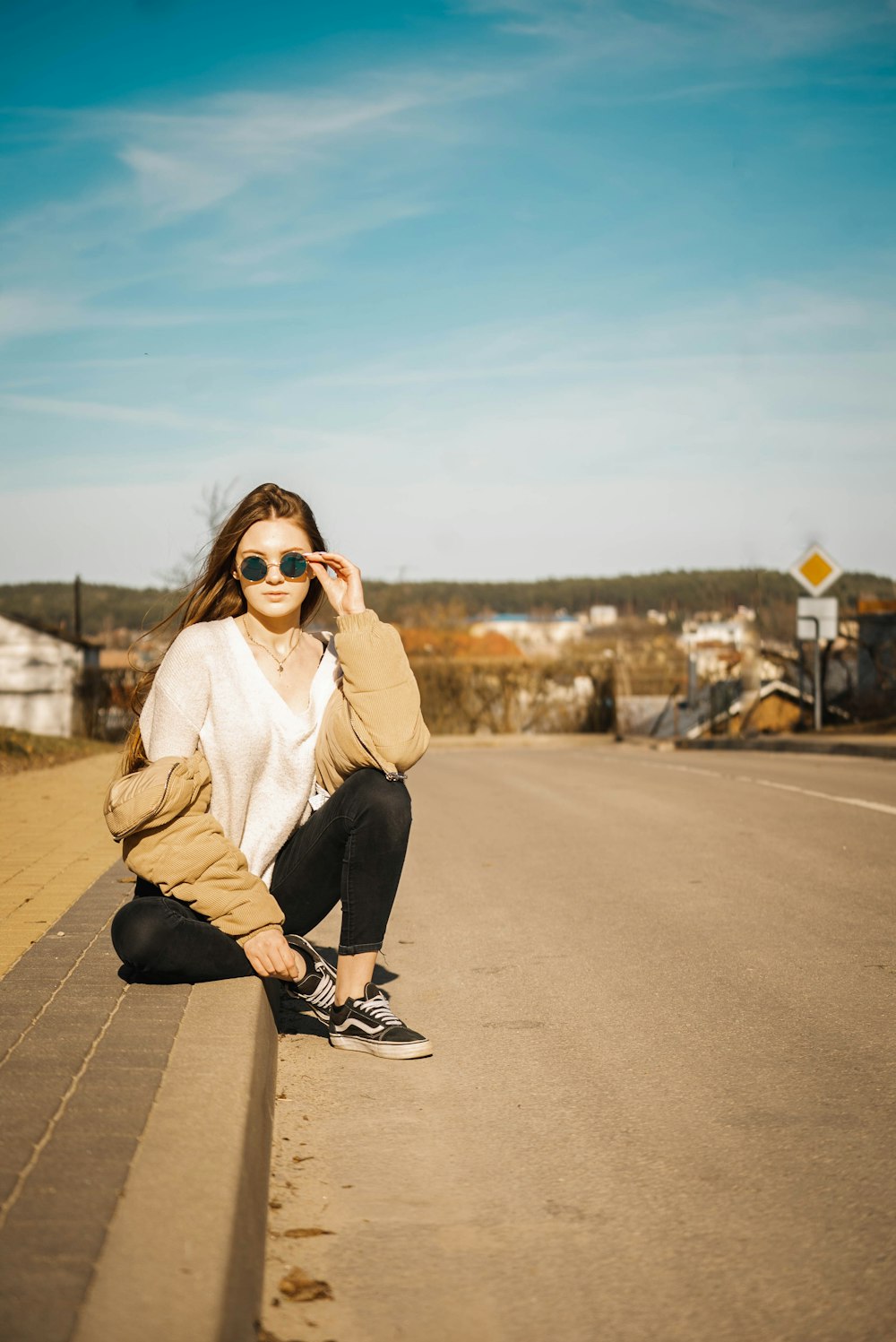 Frau hält ihre Sonnenbrille, während sie in der Nähe der Straße sitzt