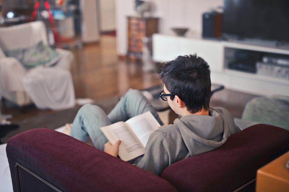 man sitting on sofa chair reading book