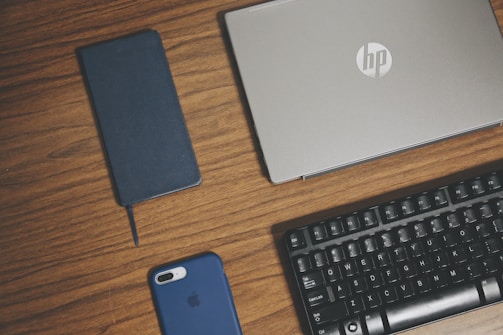 gray HP laptop, smartphone, and keyboard on brown surface