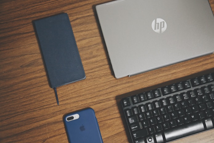 gray HP laptop, smartphone, and keyboard on brown surface
