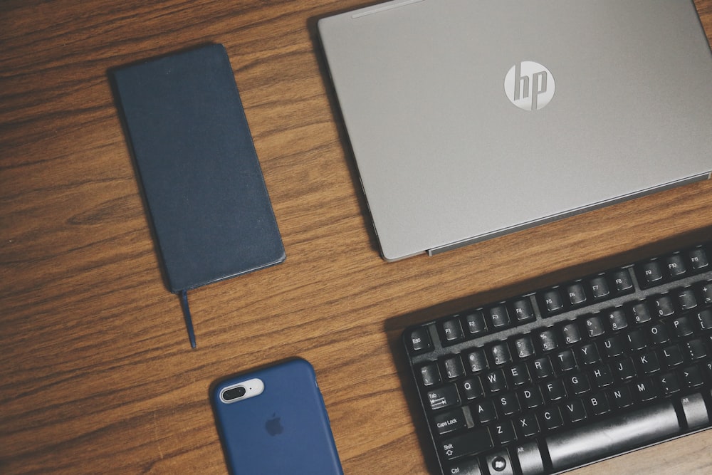 茶色の表面に灰色のHPラップトップ、スマートフォン、キーボード