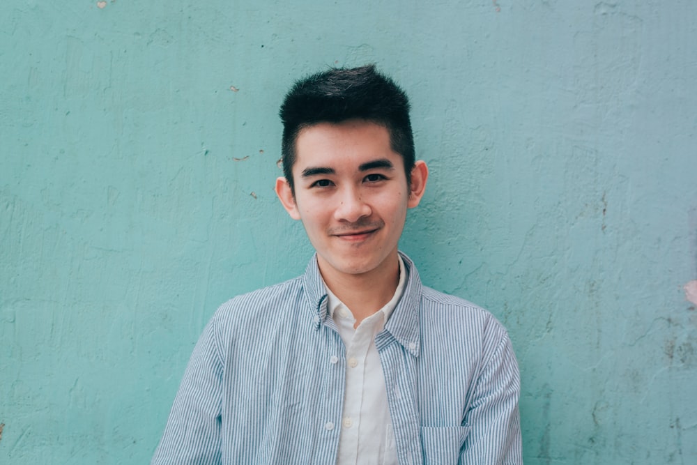 man wearing blue white stripe shirt leaning on the wall