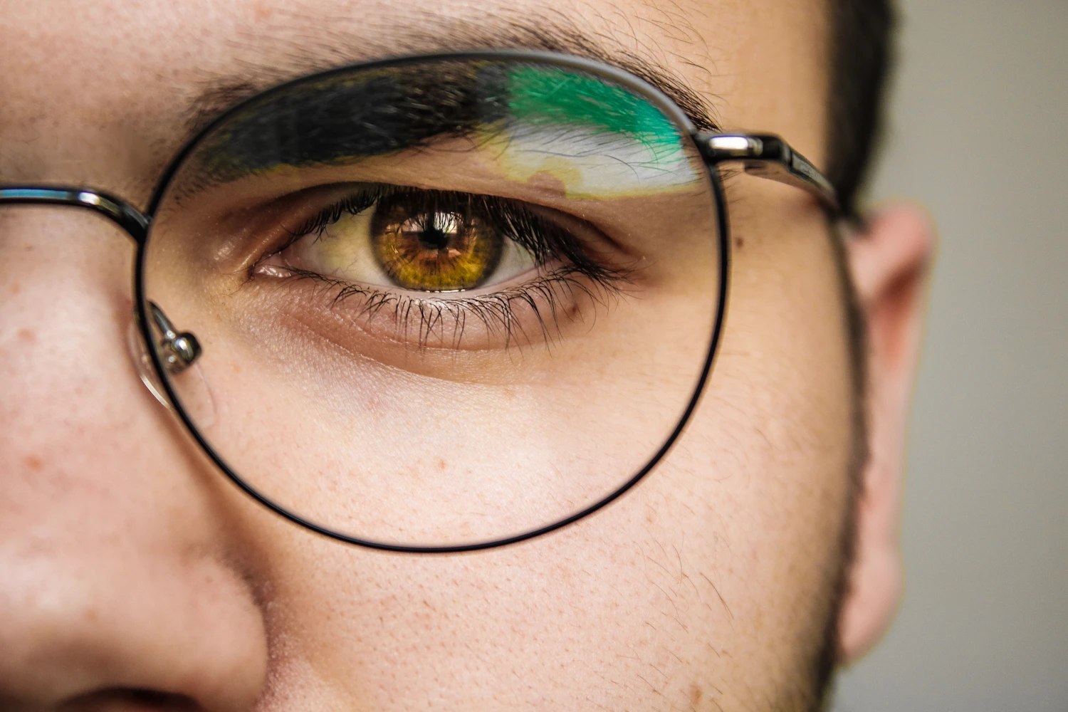 An extreme close view of one eye behind the thin round rim of a pair of glasses