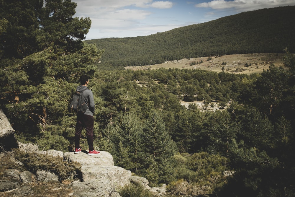 man standing on rocky hill viewing tall trees