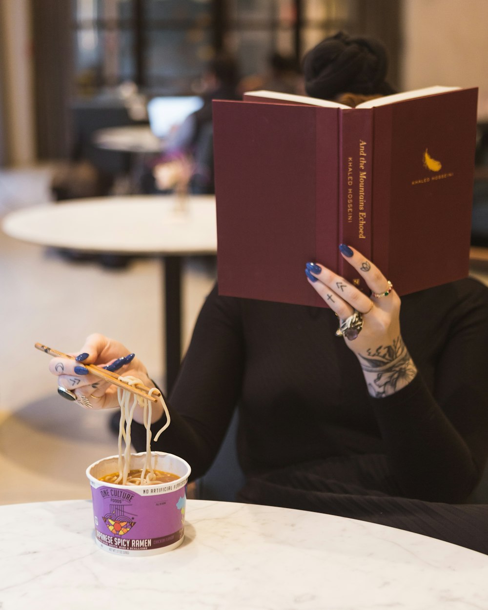 Frau sitzt am Tisch und liest Bücher, während sie Nudeln isst