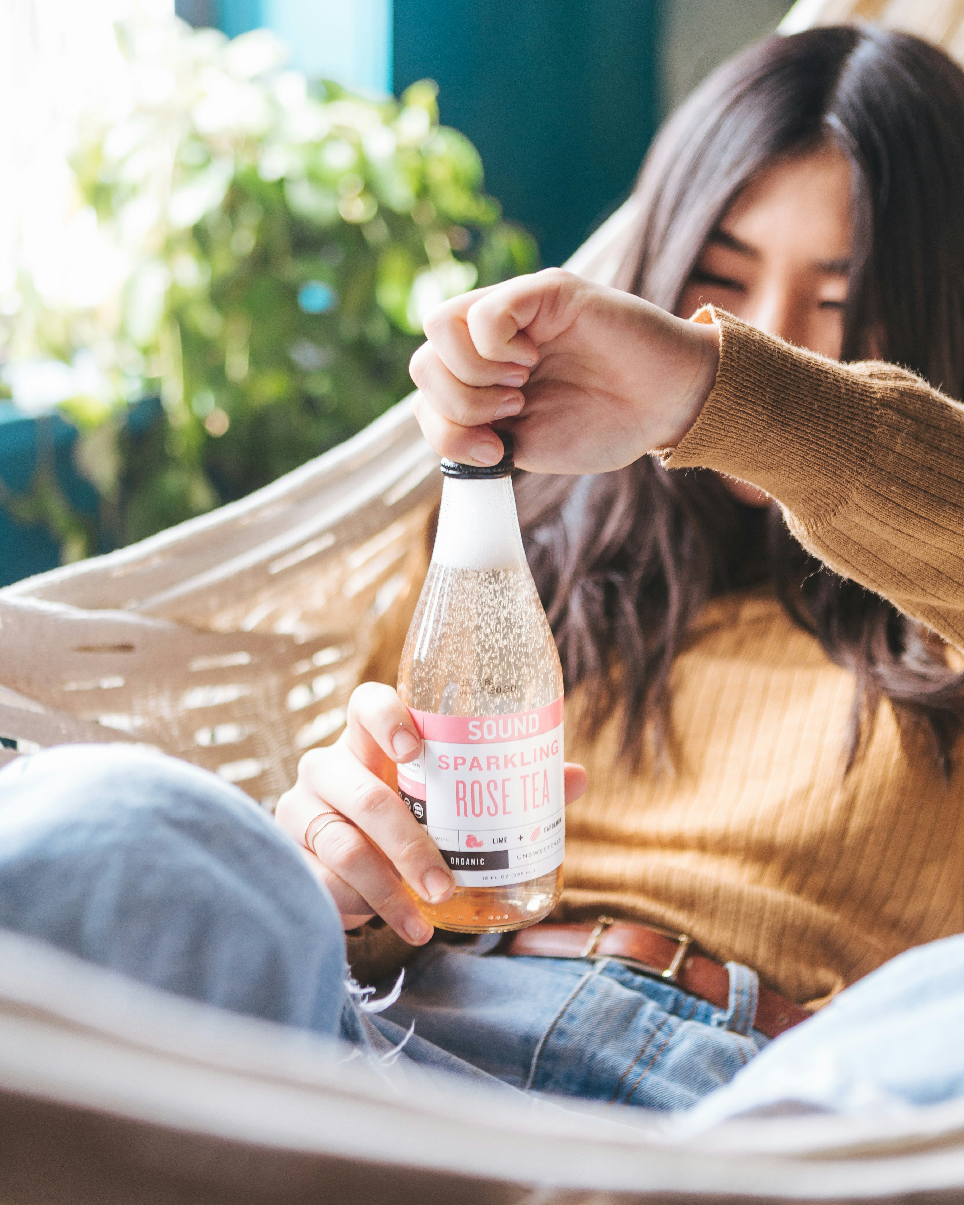 woman lying on hammock while opening labeled bottle